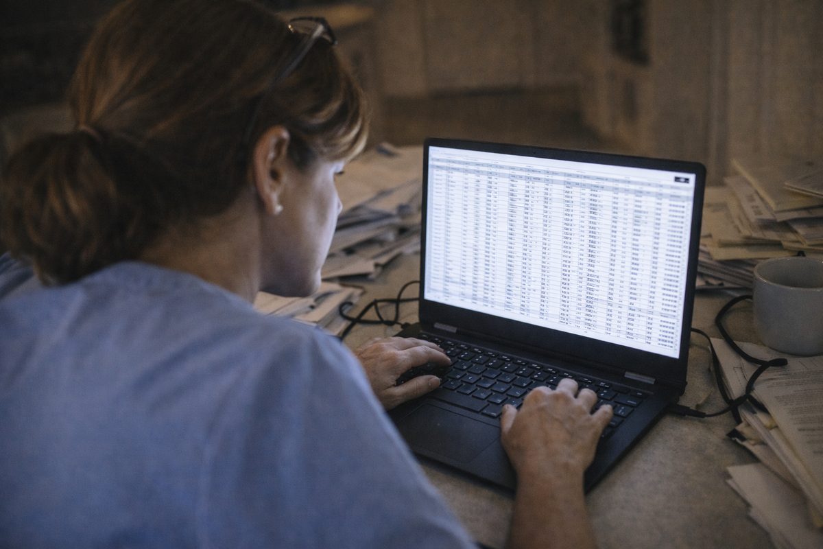 Clinician working at laptop viewing a dense spreadsheet of practice data, struggling to extract insights